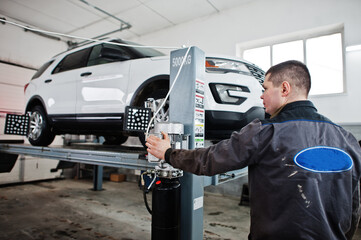 Auto mechanic sets american SUV car for diagnostics and configuration camber check in workshop of service station..