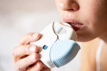Woman use asthma inhaler at home, close up.