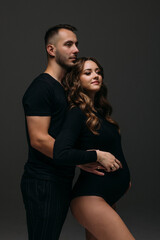 Handsome young pregnant couple posing on dark background.