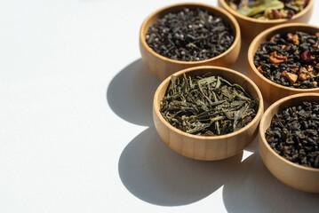Different types of green, black and herbal tea in a wooden bowl. Variety of dry leaves and flowers. Organic high-quality ingredients for a drink. Soft focus on one bowl