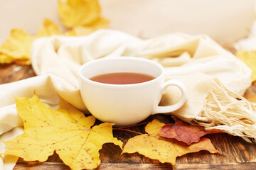 autumn leaves with a cup of tea or coffee next to a scarf on a wooden background with copy space