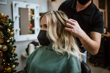 Fototapeta premium Beautiful hairstyle of woman after dyeing hair and making highlights in hair salon. She is wearing protective face mask as protection against virus pandemic.
