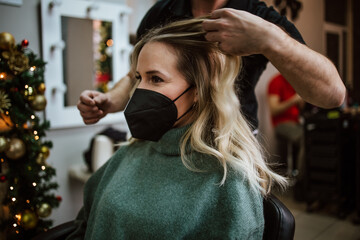 Beautiful hairstyle of woman after dyeing hair and making highlights in hair salon. She is wearing protective face mask as protection against virus pandemic.