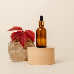 Amber glass dropper bottle of serum on podium with stone and autumn leaf at the background, natural skincare, organic moisturizing facial oil, minimal aesthetic concept