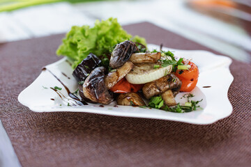 Grilled vegetables on a light background. Warm mushrooms, eggplant, peppers, onions and lettuce leaves