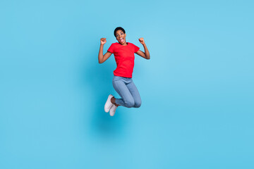 Fototapeta na wymiar Photo of lucky excited short hair human wear red t-shirt jumping high rising fists isolated blue color background