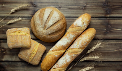 round rye bread, ciabatta buns, wheat baguette with wheat ears on a wooden background. top view