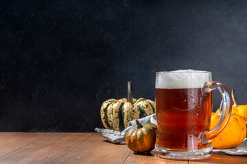 Dark frothy  pumpkin ale in beer glass mug, autumn homemade alcohol drink, with small pumpkins on wooden kitchen table 