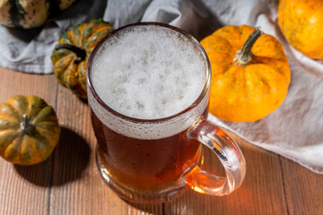 Dark frothy  pumpkin ale in beer glass mug, autumn homemade alcohol drink, with small pumpkins on wooden kitchen table 