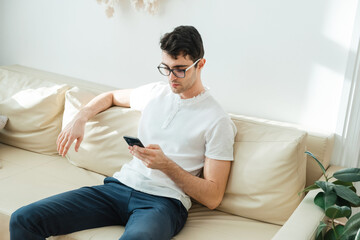 Portrait of a male freelancer who is always in touch at home. Handsome focused young man using his smartphone while sitting on the couch