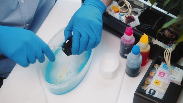 Video. Master repairs inkjet printer. Professional specialist washes printer parts from syringe. Hands with gloves close-up. Type of maintenance and repair of office equipment..