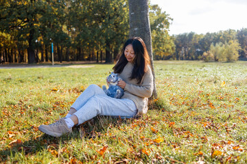 Adorable young rabbit and woman sit together outdoor in autumn forest. Asian woman wear warm sweater with pet in relax and calm.