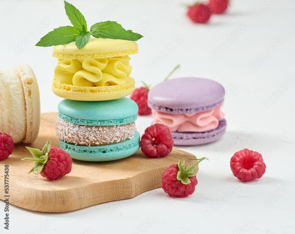 Poster stack of multicolored macaroons and red raspberries on a white background.