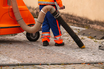 Worker collecting leaves from the street with a suction industrial machine. Public cleaning...