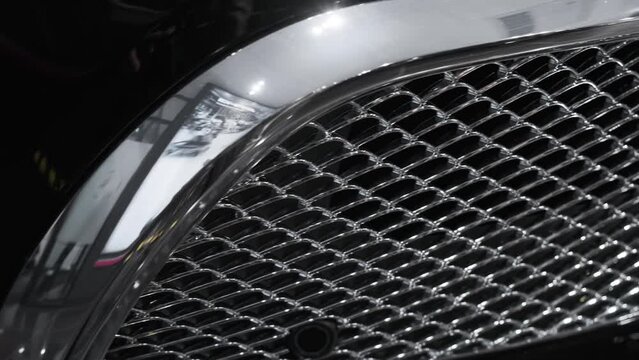 Closeup cinematic view of chrome plated decorative grille in front bumper of modern luxury prestigious SUV in black at dealer showroom. Sale of new cars, tuning, detailing, service