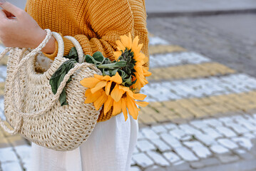 A girl in a knitted sweater with a wicker bag with sunflowers crosses the road on a pedestrian crossing.