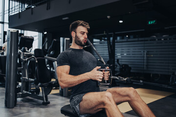 Fototapeta na wymiar Good looking handsome male athlete exercising in modern fitness gym. Dark muddy light with strong shadows. Indoors sport concept.