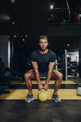 Good looking handsome male athlete exercising in modern fitness gym. Dark muddy light with strong shadows. Indoors sport concept.