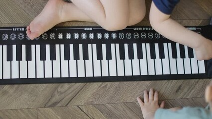 children hands fingers baby hands electronic piano sitting floor naked legs feet. two little unrecognizable caucasian children trying to play soft piano keys elder kid push buttons toddler child looks - Powered by Adobe