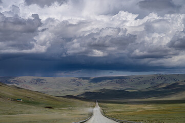 Fototapeta na wymiar Road going into the horizon in Mongolia. Clouds in the sky.
