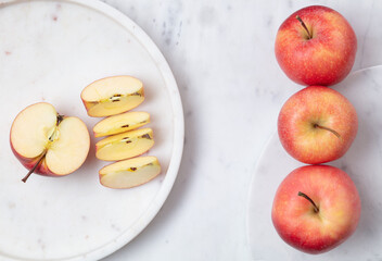 Naklejka na ściany i meble Whole and sliced red delicious apples in a white marble plate. Flat lay