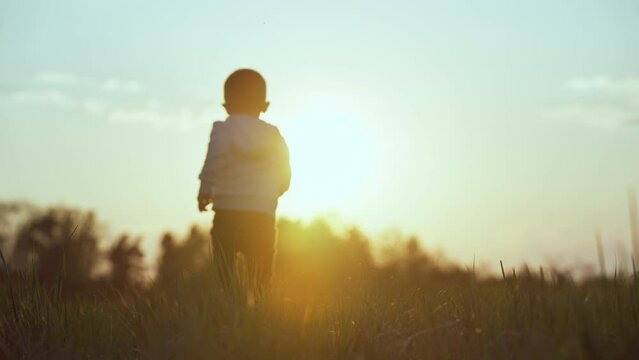 Slow motion video of a happy free child running across the field. A feeling of happiness and freedom in nature at sunset. The boy runs on the grass. High quality 4k footage