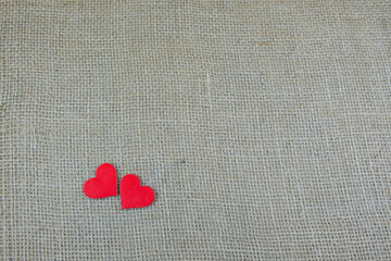 two red hearts on a gray, beige background from a linen texture. natural cotton burlap