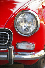 Round and chrome headlight on a red vintage car.