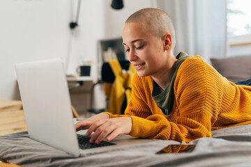 young bald female laying in her room and using laptop computer
