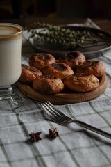 Scones on a wooden plate with fork, coffee and milk in a glass cup. On a white checkered towel
