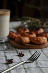 Scones on a wooden plate with fork, coffee and milk in a glass cup. On a white checkered towel