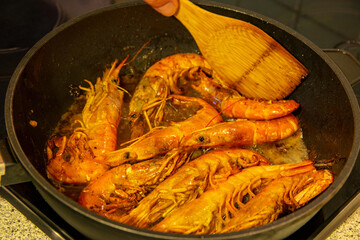 Argentinian red prawns. The argentine red fried shrimps in a pan and a hand with a wooden spoon....