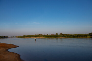 A fly-fishing fisherman on the river in summer.fly fishing fisherman in a gray jacket fishing in the middle of the river in the river in summer.copy space.bright advertising of fishing gear production