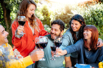 Group of friends having dinner outdoors toasting with red wine in the backyard of the restaurant -...