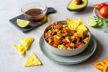 Cowboy caviar is traditional Mexican vegetable salad in bowl with ingredients, dip and nachos on grey background
