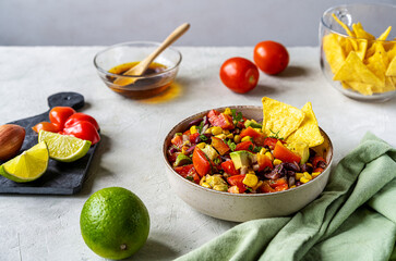 Cowboy caviar is traditional Mexican vegetable salad in bowl with ingredients and nachos on concrete background 