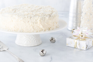 A coconut covered carrot cake surrounded by decorations all in white.