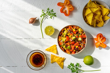 Traditional Mexican vegetable salad . cowboy caviar in bowl with ingredients and nachos on white wooden table with ingredients