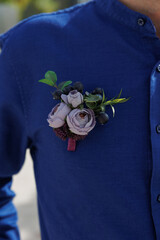 the groom in a blue shirt with a boutonniere of pale purple artificial roses