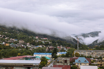 Fototapeta na wymiar Fog over the city in the mountains. Picturesque autumn landscape. Smoking pipe boiler room pipe on the background of clouds. Sochi, Russia.