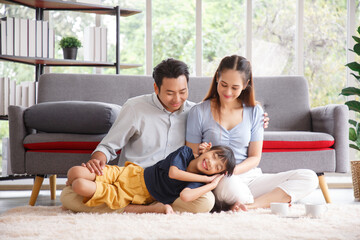 Portrait of a happy young family. Mom; dad and daughter look at the camera and smile. The faces of Asian parents and their child in living room. Family funning in living room.