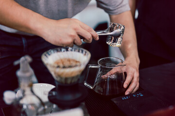 Obraz na płótnie Canvas Barista making iced coffee by putting an ice into a glass jar with black freshly brewed coffee.