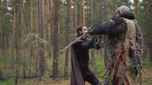 Knight falls down after monster strike in coniferous forest slow motion. Middle aged soldier losses in battle with demon at reconstruction. Tolkienist games