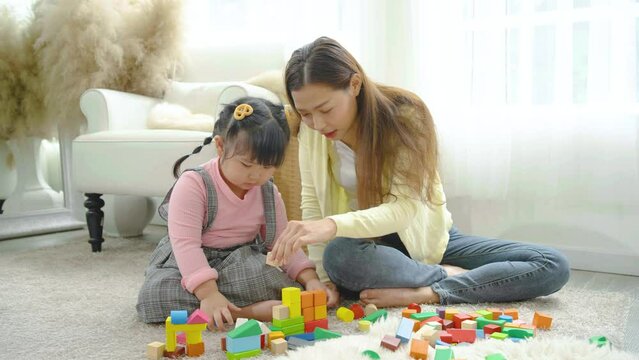 Young asian mother and little daughter enjoy to play puzzle wood toy together in area of living room of their house and they look happiness, childhood and motherhood concept