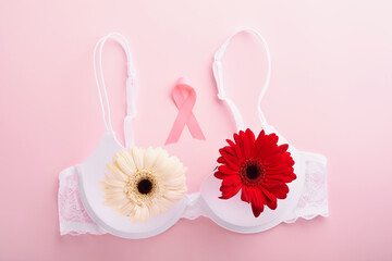 Breast Cancer Awareness Ribbon. White and red bra, gerberas with pink ribbon tape lying on female bra on backgrounds. Breast cancer awareness and October Pink day, world cancer day. Top view. Mock up