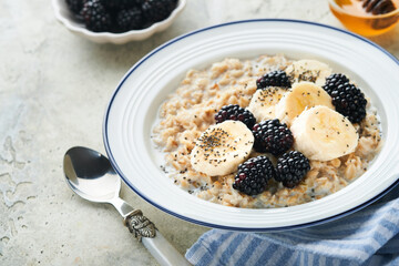Oatmeal. Bowl of oatmeal porridge with blackberry, bananas and chia seeds on gray concrete old table background. Top view in flat lay style. Natural ingredients Hot and healthy breakfast and diet food