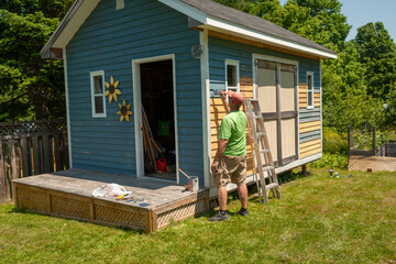 Man painting the exterior of a backyard shed
