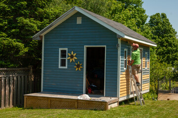 Man painting the exterior of a backyard shed - obrazy, fototapety, plakaty