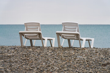 Two white plastic sun beds on a pebble beach near the sea coastline. Copy space.