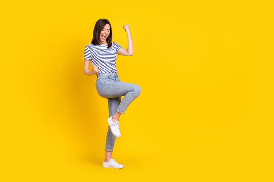 Full size photo of satisfied overjoyed lady raise arm leg yelling yeap win lottery stand empty space isolated on yellow color background